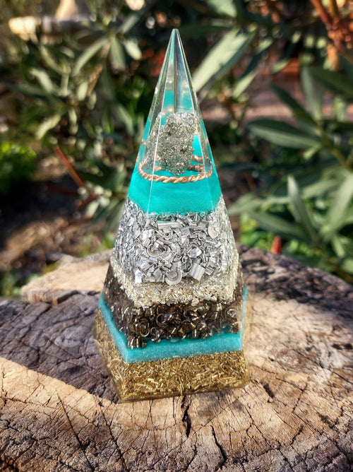 Handcrafted Azure Pyrite Pentagon Orgonite Pyramid with turquoise layers, pyrite crystal core, metal shavings and sacred geometry design, placed outdoors on natural wood surface