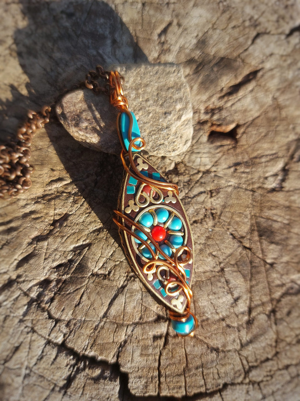 Tibetan turquoise pendant with copper wire ornament resting on wood