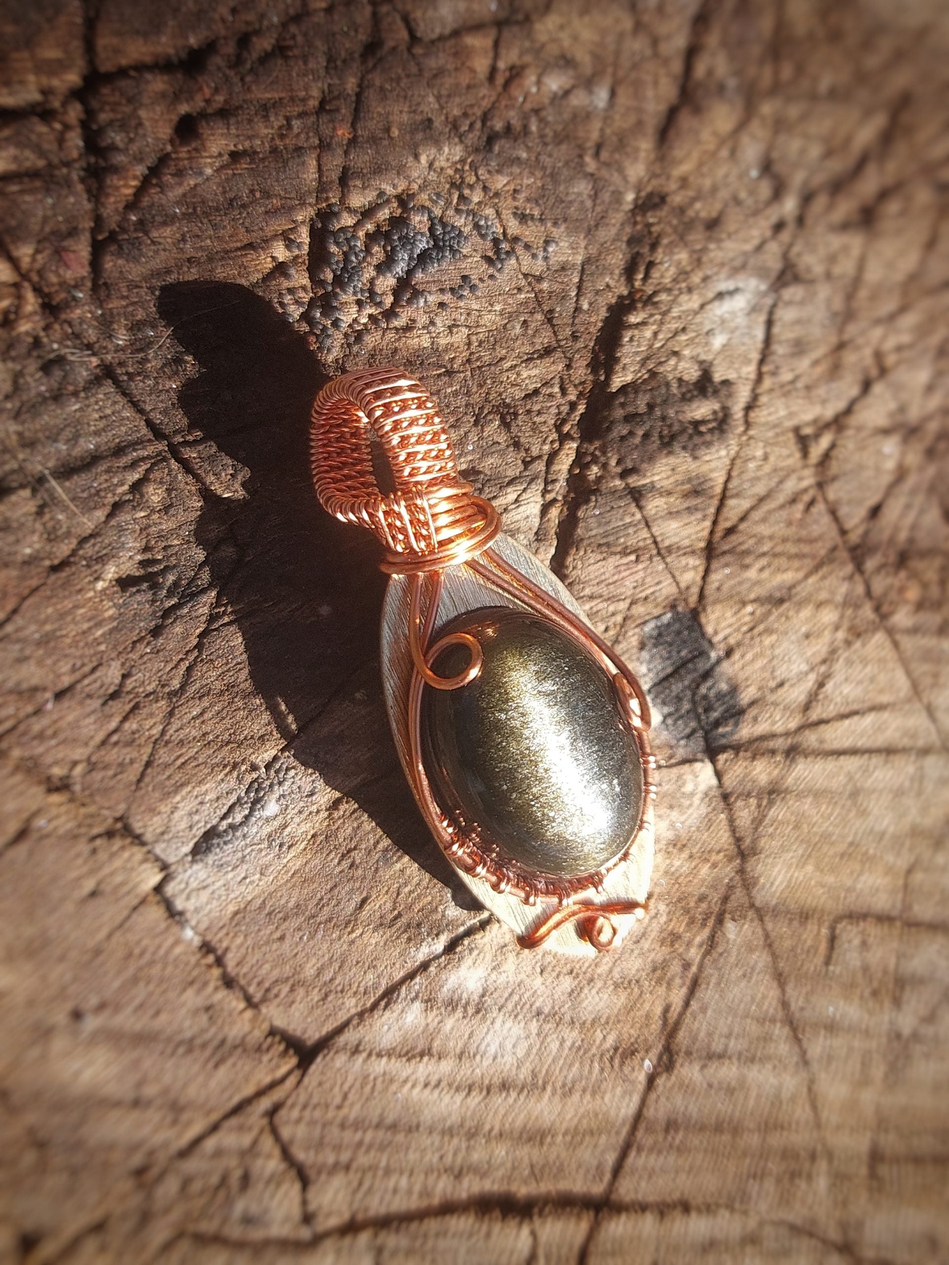 Golden obsidian pendant wrapped in copper wire resting on wood surface
