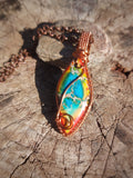 Calsilica pendant wrapped in copper wire resting on wood