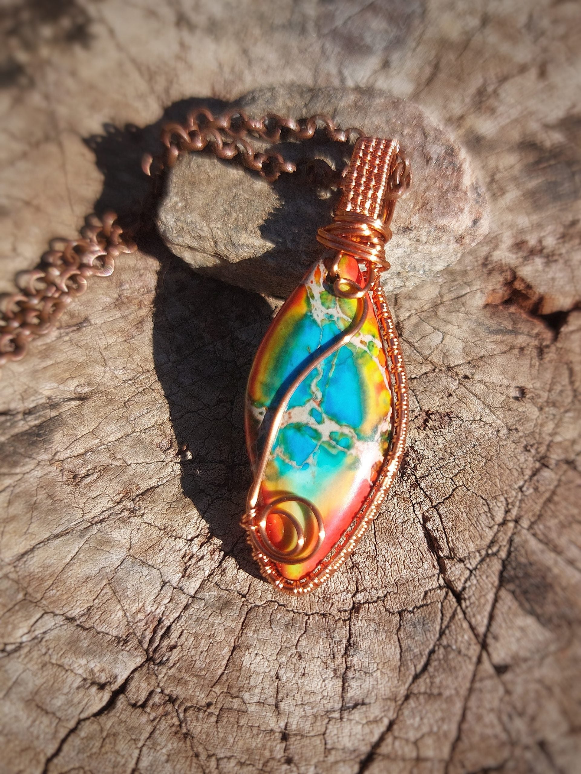 Calsilica pendant wrapped in copper wire resting on wood
