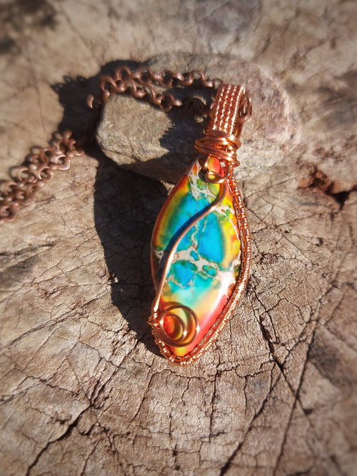 Calsilica pendant wrapped in copper wire resting on wood