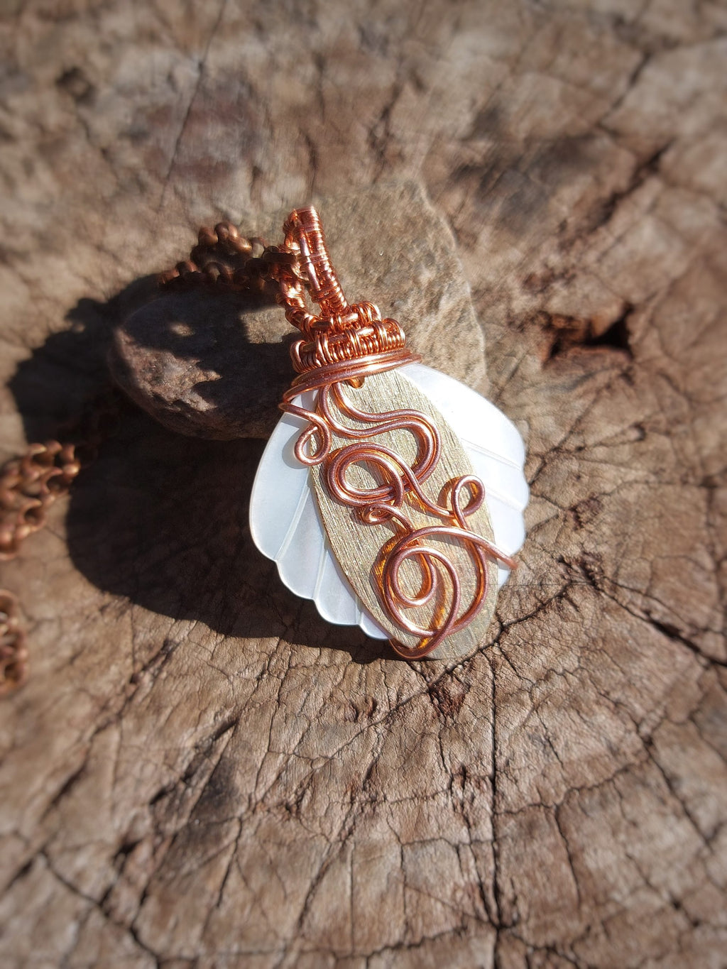Mother of pearl pendant wrapped in copper and brass wire on wood surface