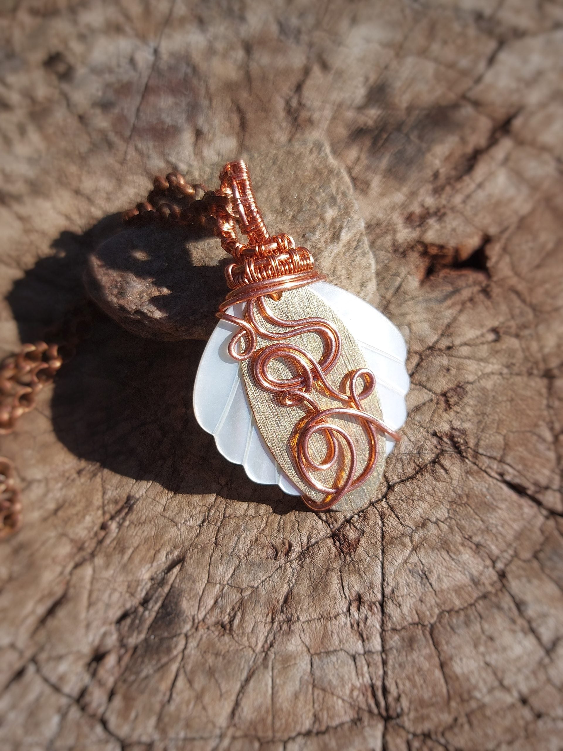 Mother of pearl pendant wrapped in copper and brass wire on wood surface