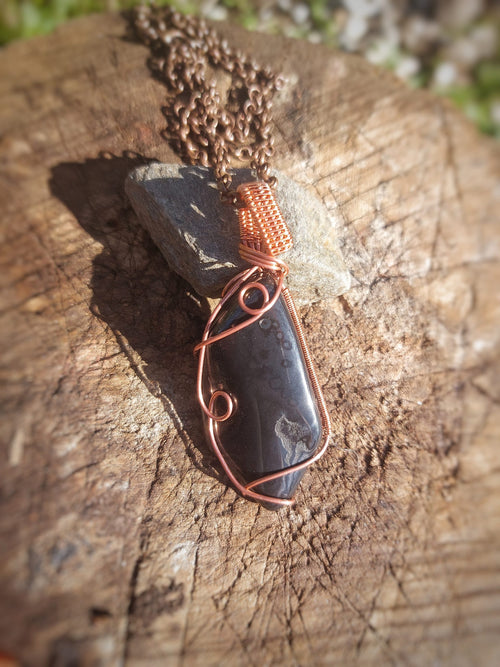 Hematiet edelsteen hanger met koper wire wrap en ketting, natuurlijke lichtinval buiten gefotografeerd