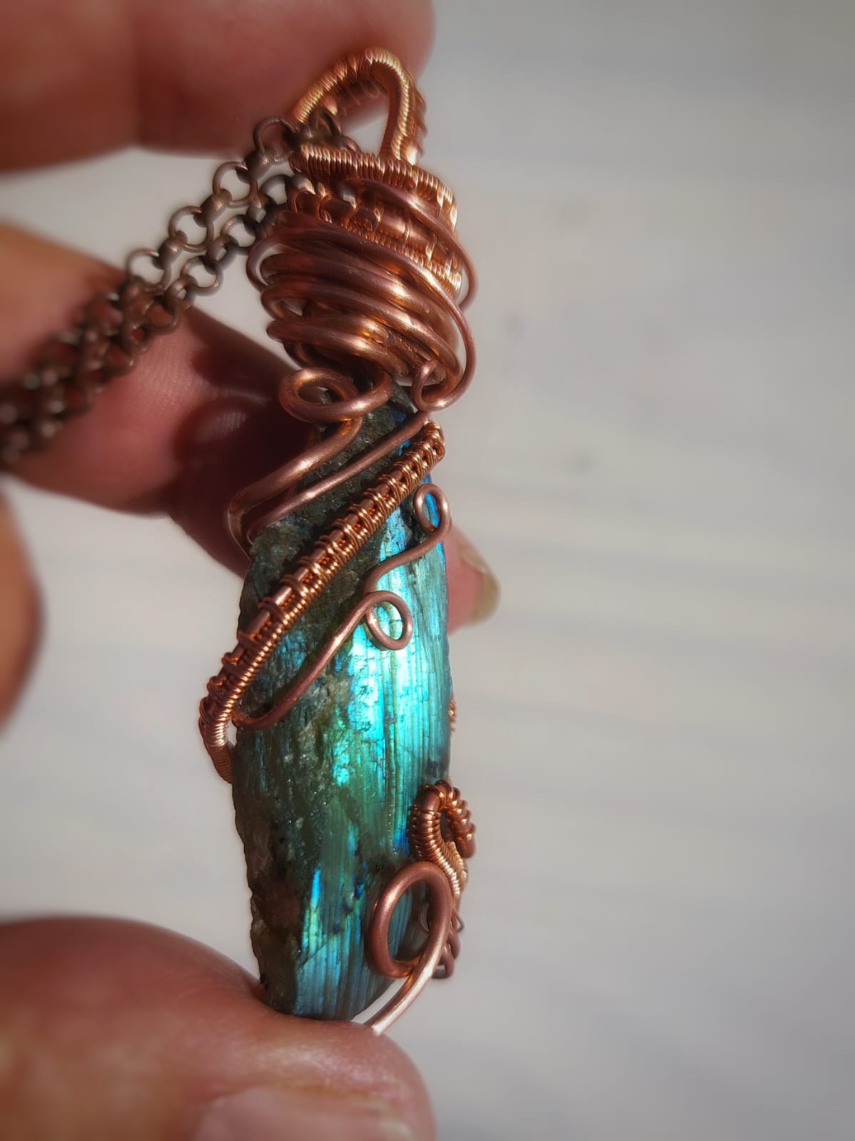 Close-up of natural labradorite crystal pendant wrapped in copper wire, showing blue green labradorescence and handmade detailing