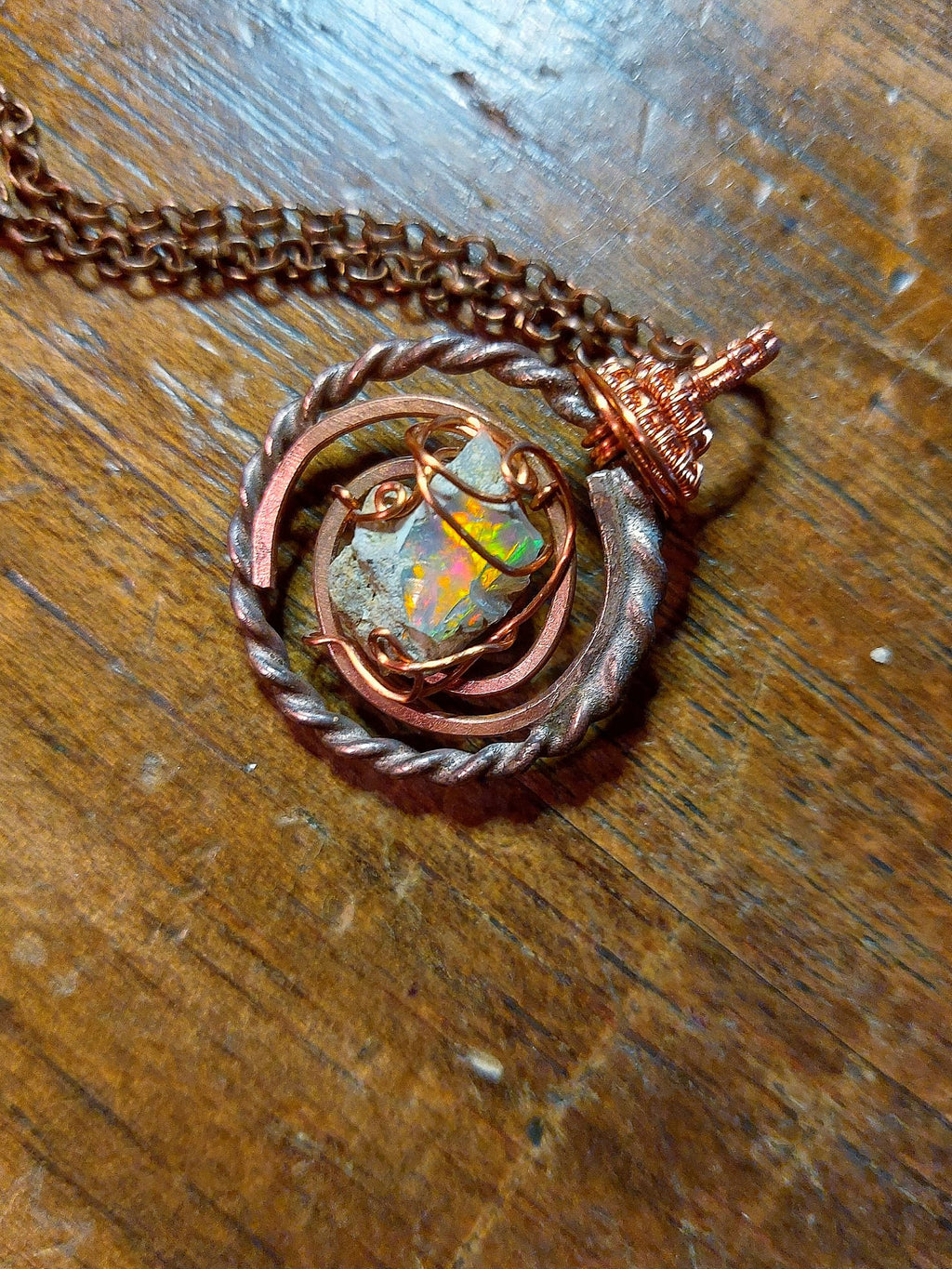 Opal energy pendant with sacred geometry ring and copper wire wrapping on wooden surface